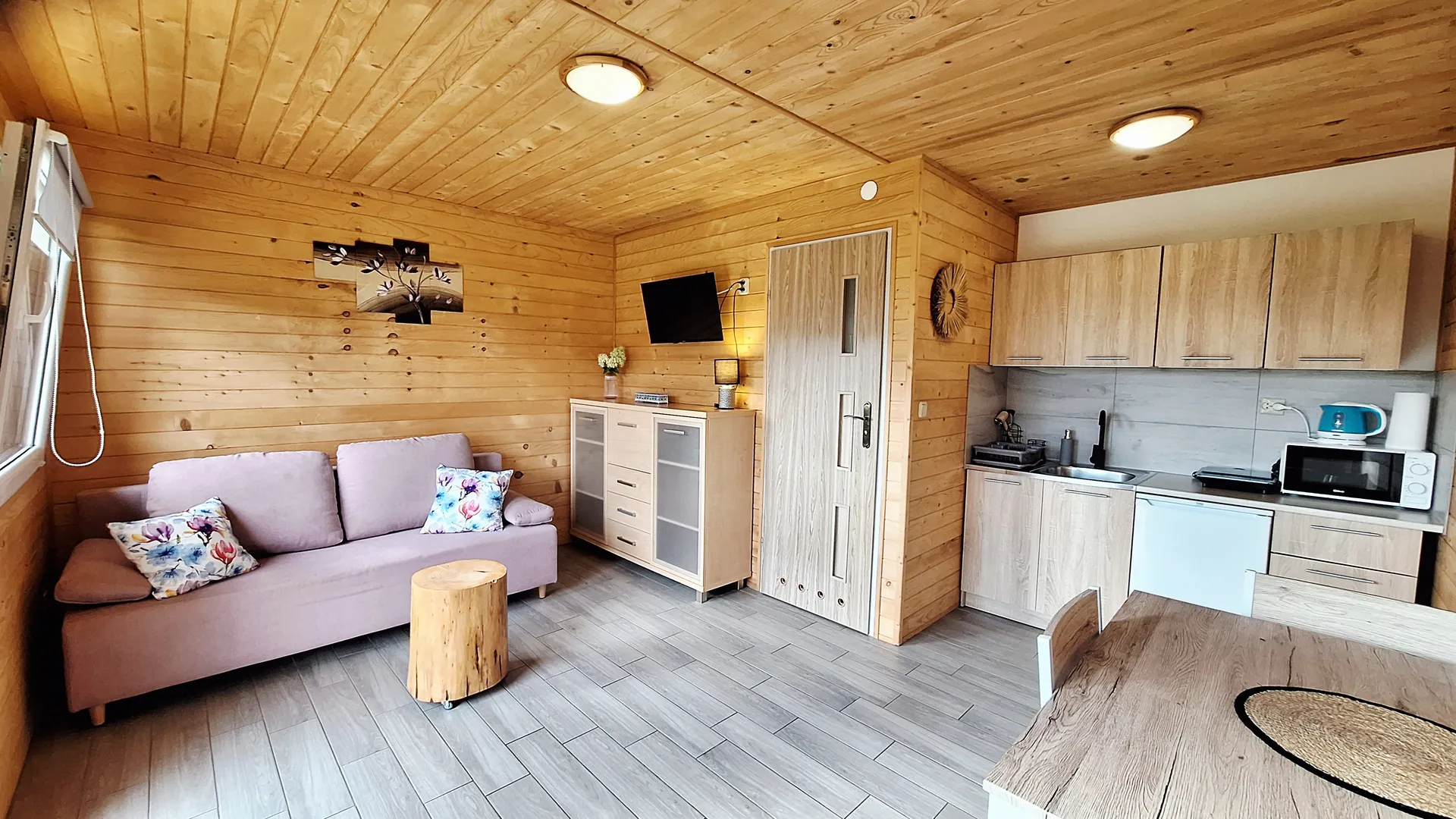 Wnętrze domku w Bieszczadach - przytulny salon z wygodną sofą, stolikiem z pnia drzewa i aneksem kuchennym